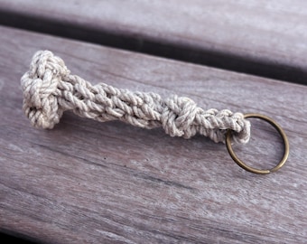 May include: A beige rope keychain with a knot at the top and a brass key ring.