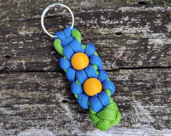 May include: A blue and green paracord keychain with two yellow beads in the shape of flowers.