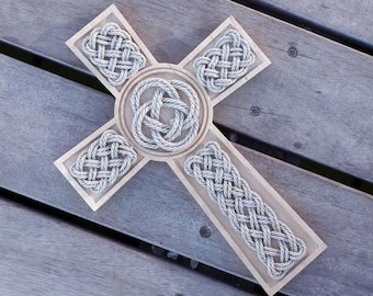 May include: A wooden cross with a Celtic knot design carved into the surface. The knots are made of a light gray rope.