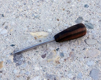 May include: A close-up of a small, wooden-handled tool with a metal shaft. The tool has a dark brown wooden handle with black stripes and a silver metal shaft.