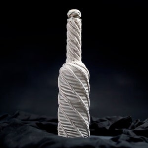 May include: A white ceramic bottle with a textured, spiral design. The bottle is sitting on a black fabric surface.
