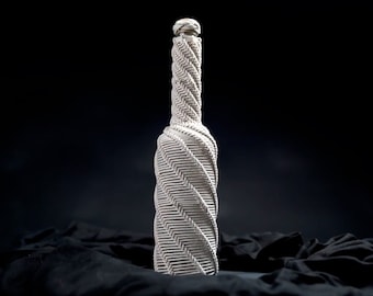 May include: A white ceramic bottle with a textured, spiral design. The bottle is sitting on a black fabric surface.