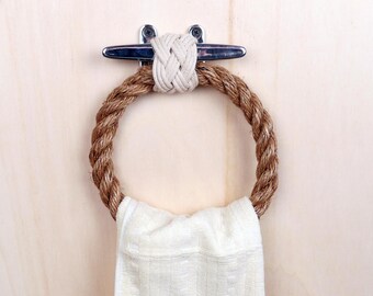 May include: A brown rope towel ring with a white towel hanging on it. The ring is attached to a wall with a silver cleat.