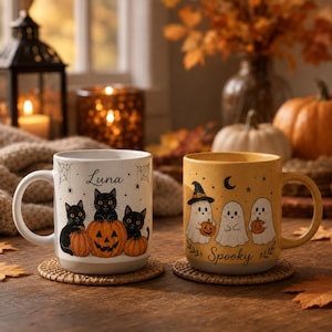 May include: Two ceramic mugs featuring Halloween designs. The left mug is white with three black cats, pumpkins, and the name Luna. The right mug is yellow with three ghosts, small pumpkins, and the word Spooky. Both mugs have handles.