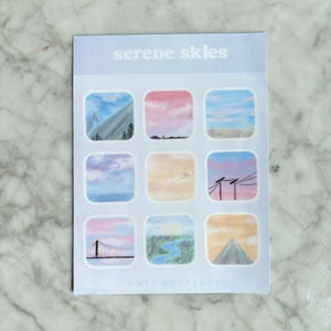 May include: A sheet of stickers with the text "serene skies" at the top. The stickers feature square illustrations of various sky scenes, including mountains, sunsets, and landscapes. The color palette includes blues, pinks, and oranges.