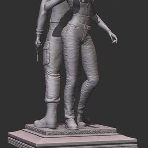 May include: A gray sculpture of two figures, a man and a woman, standing close together. The woman is holding a gun and pointing. The man is behind her, also holding a gun. They stand on a decorative base.