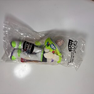 May include: A green and white Buzz Lightyear plush toy from the movie Toy Story. The toy is packaged in a clear plastic bag with a Burger King logo and the words "Toy Story" printed on it.