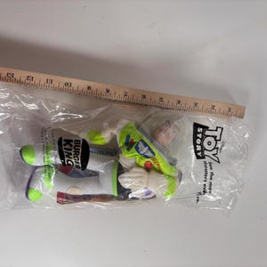 May include: A green and white Buzz Lightyear plush toy from the movie Toy Story. The plush toy is packaged in a clear plastic bag with a Burger King logo and the words "See the movie in theaters everywhere."