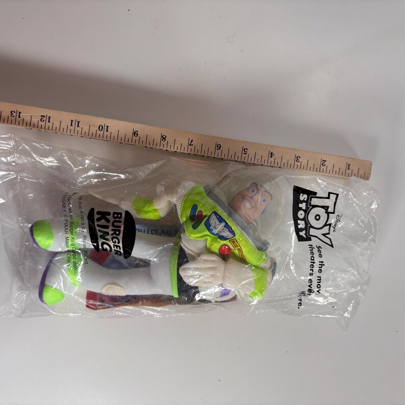 May include: A green and white Buzz Lightyear plush toy from the movie Toy Story. The plush toy is packaged in a clear plastic bag with a Burger King logo and the words "See the movie in theaters everywhere."