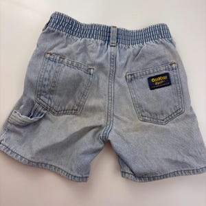 Puede incluir: Pantalones cortos de mezclilla azul claro con cintura el&aacute;stica y un parche "OshKosh B'Gosh" en el bolsillo trasero.