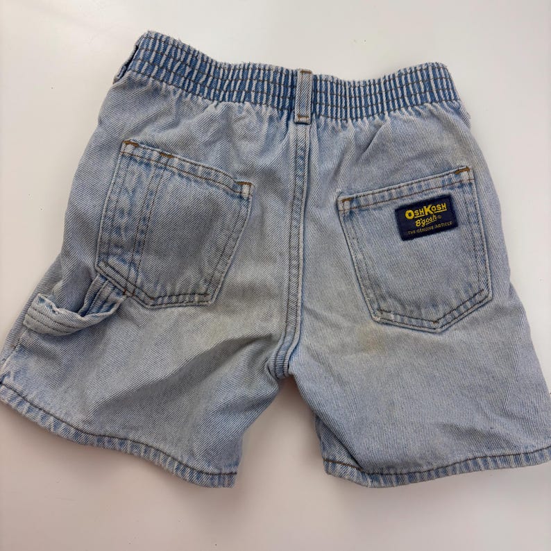 Puede incluir: Pantalones cortos de mezclilla azul claro con cintura el&aacute;stica y un parche "OshKosh B'Gosh" en el bolsillo trasero.