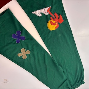 May include: Green sweatpants with colorful embroidered flowers and a sun with a red palm tree on one leg.