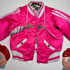 May include: Bright pink satin jacket with white stripes on the sleeves and trim. The jacket has the words "Rock Fever" embroidered on the front. The interior lining features a zebra print.