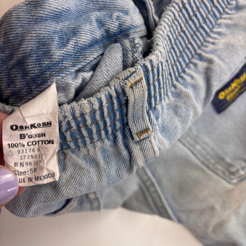 Puede incluir: Pantalones cortos de mezclilla azul claro con una etiqueta blanca que dice "OSHKOSH B'GOSH 100% COTTON 93176 6 372501 RN 96367 Size: 5R DE IN MEXICO".