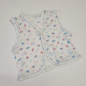 Könnte beinhalten: Weißes ärmelloses Baby-Jäckchen mit einem blauen und rosa Muster aus Babyspielzeug und Flaschen. Das Jäckchen hat einen Knopfverschluss.