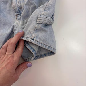 Puede incluir: Pantalones cortos de mezclilla azul claro con un solo bolsillo en la pierna derecha. Los pantalones cortos est&aacute;n doblados y la tela est&aacute; ligeramente desgastada.