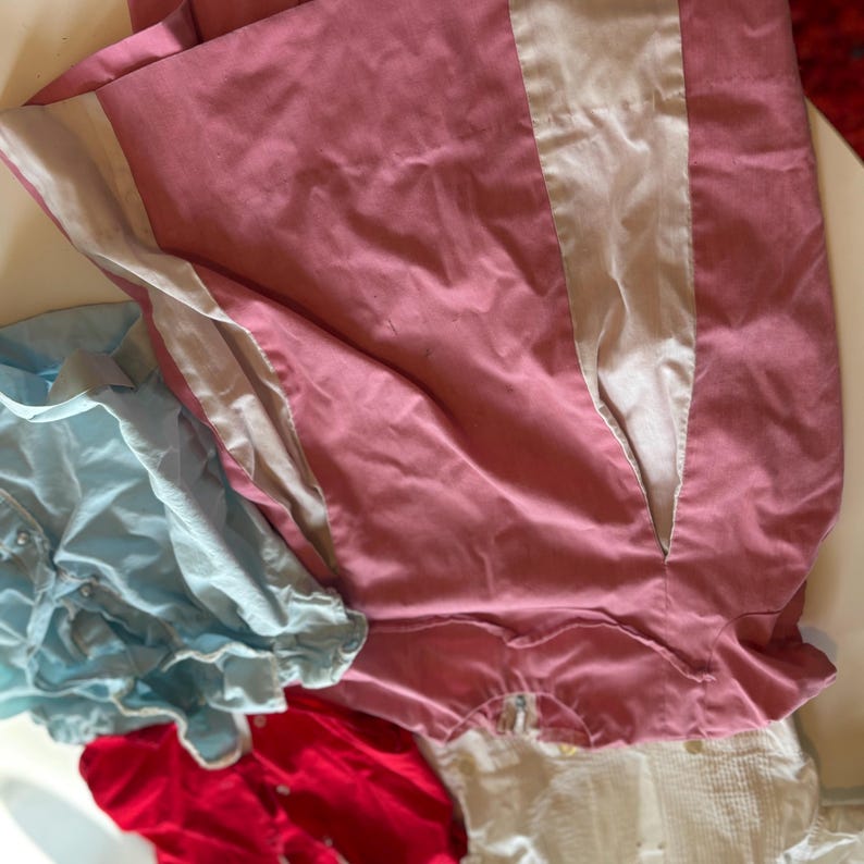 K&ouml;nnte beinhalten: Sortiment an Kinderkleidung in verschiedenen Farben. Ein rosa Kleidungsst&uuml;ck mit wei&szlig;em Einsatz befindet sich oben. Weitere Artikel sind ein hellblaues Oberteil, ein rotes Oberteil und ein wei&szlig;es Oberteil. Die Stoffe scheinen weich und leicht zu sein.