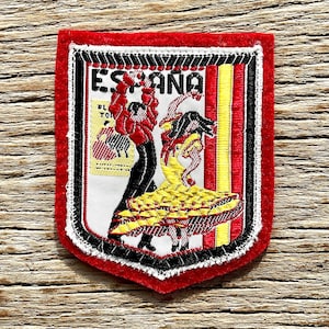 Può includere: Toppa ricamata con bordo rosso e la scritta "España" in alto. La toppa presenta un'illustrazione colorata di ballerini di flamenco. Il design include elementi neri, gialli, rossi e bianchi, con un bordo cucito in bianco e nero.