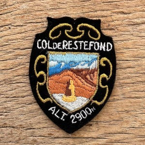 Op de afbeelding: Zwarte geborduurde patch met gouden rand en de tekst "COLDERESTEFOND" in het wit. De patch toont een berglandschap met blauwe, bruine en oranje kleuren en de tekst "ALT 2900m".