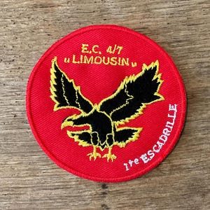 Op de afbeelding: Een ronde rode patch met een zwart adelaarsymbool en gele accenten. De patch bevat de tekst "E.C. 4/7 LIMOUSIN" en "1re ESCADRILLE" in witte letters, waarschijnlijk een militair of luchtvaartinsigne.