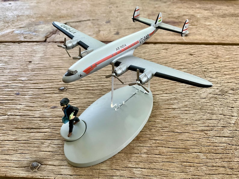 K&ouml;nnte beinhalten: Ein silbernes Modellflugzeug mit der Aufschrift "Air India" und "VT-DAD" auf dem Rumpf. Das Flugzeug hat rote und schwarze Akzente und ist auf einem grauen St&auml;nder montiert. Eine kleine Figur rennt auf dem St&auml;nder.