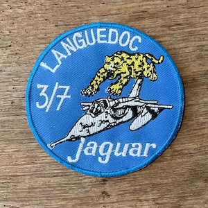 Op de afbeelding: Een ronde, blauwe patch met een geel en zwarte jaguar boven een wit straalvliegtuig. De patch heeft witte tekst met de woorden "LANGUEDOC", "3/7" en "Jaguar".