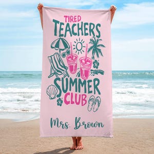 May include: A pink beach towel with the words "Tired Teachers Summer Club" in teal and pink. The towel features illustrations of a beach umbrella, sunglasses, drinks, a beach chair, a seashell, flowers, and flip-flops. The name "Mrs. Brown" is printed at the bottom.