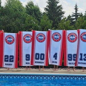 Peut inclure: Une rang&eacute;e de banni&egrave;res blanches et rouges avec des num&eacute;ros et des noms bleus, arborant un logo circulaire. Les banni&egrave;res sont tenues devant une piscine. Les num&eacute;ros et les noms sont en bleu. Les banni&egrave;res ont une bordure rouge et une bande rouge au milieu.