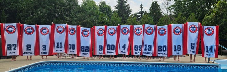 Peut inclure: Une rang&eacute;e de banni&egrave;res blanches et rouges avec des num&eacute;ros et des noms bleus, arborant un logo circulaire. Les banni&egrave;res sont tenues devant une piscine. Les num&eacute;ros et les noms sont en bleu. Les banni&egrave;res ont une bordure rouge et une bande rouge au milieu.