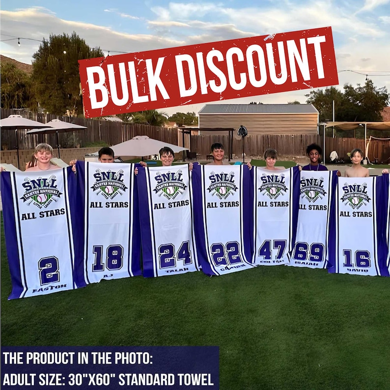 Puede incluir: Un grupo de personas sostienen toallas blancas y azules con tem&aacute;tica de b&eacute;isbol. Cada toalla tiene un n&uacute;mero y el texto "SNLL All Stars". Las toallas miden 76 cm x 152 cm, con las palabras "Bulk Discount" en una pancarta roja.