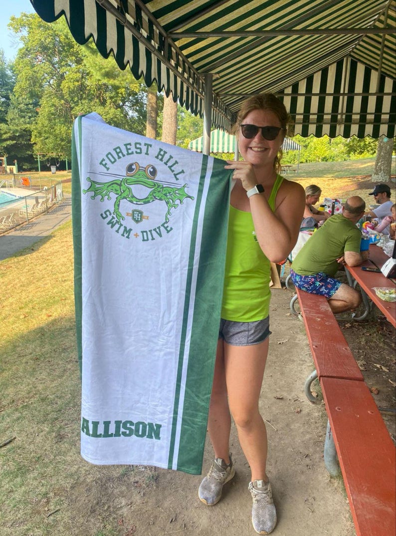 Puede incluir: Toalla de playa blanca y verde con el texto "FOREST HILL SWIM + DIVE" y un dise&ntilde;o de rana. La toalla tiene rayas verdes y el nombre "ALLISON".