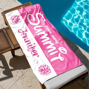 May include: A personalized pink and white beach towel with the name "Jennifer" and "Summit" printed in white script. The towel also features a pom-pom graphic and the year "2020". The towel is lying on a wooden lounge chair next to a pool.