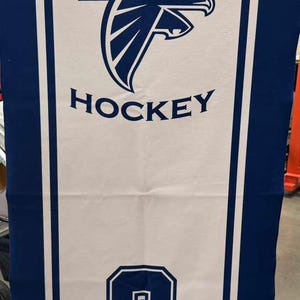 Peut inclure: Serviette de hockey blanche et bleue. Le mot "DANVERS" est en haut, avec un logo de faucon bleu et le mot "HOCKEY" en dessous. Le num&eacute;ro "3" est dans un encadr&eacute; bleu, avec le nom "GODFRIED" en dessous.