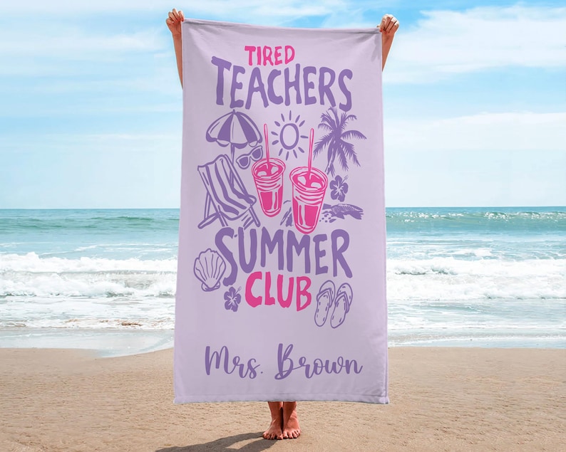 May include: A lilac beach towel with the words "Tired Teachers Summer Club" in purple and pink. The towel has illustrations of a parasol, sunglasses, drinks, a deckchair, and a palm tree. The name "Mrs. Brown" is printed at the bottom.