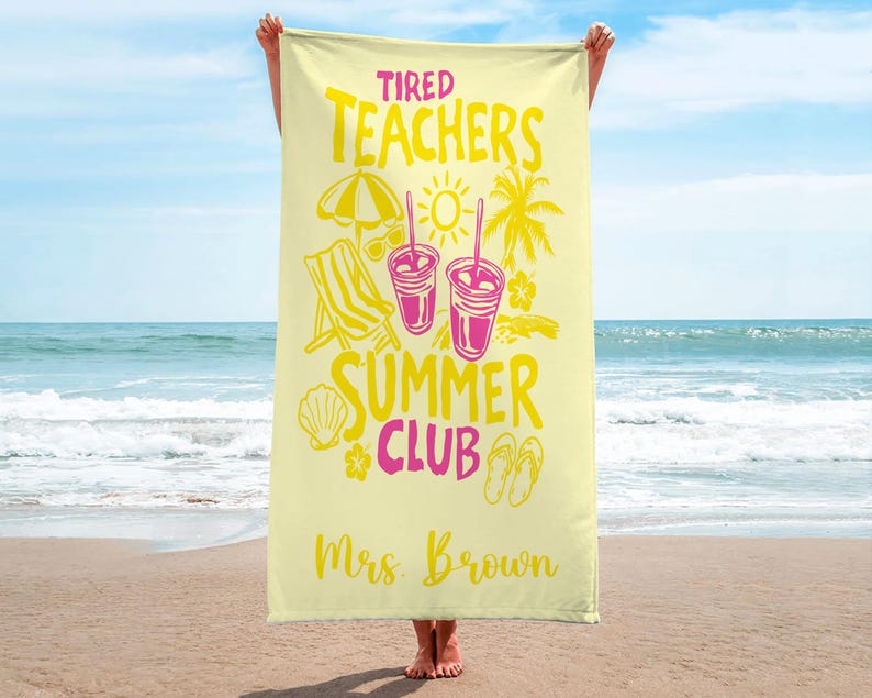 May include: A pale yellow beach towel with the text "Tired Teachers Summer Club" in yellow and pink. The towel design includes illustrations of a beach umbrella, sunglasses, a beach chair, drinks, a seashell, flowers, and flip-flops. The name "Mrs. Brown" is printed.