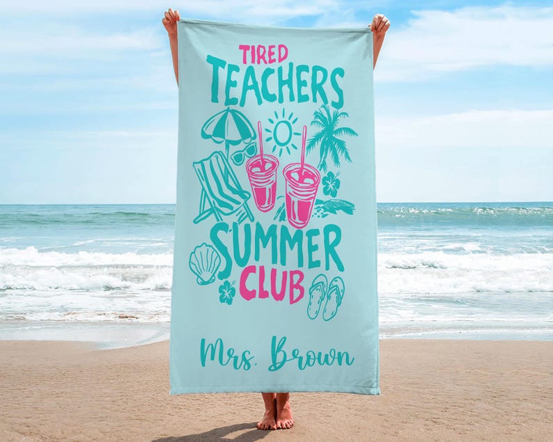May include: A light blue beach towel with the words "Tired Teachers Summer Club" in teal and pink. The towel features illustrations of a beach umbrella, sunglasses, drinks, a chair, and a seashell. The name "Mrs. Brown" is printed at the bottom.