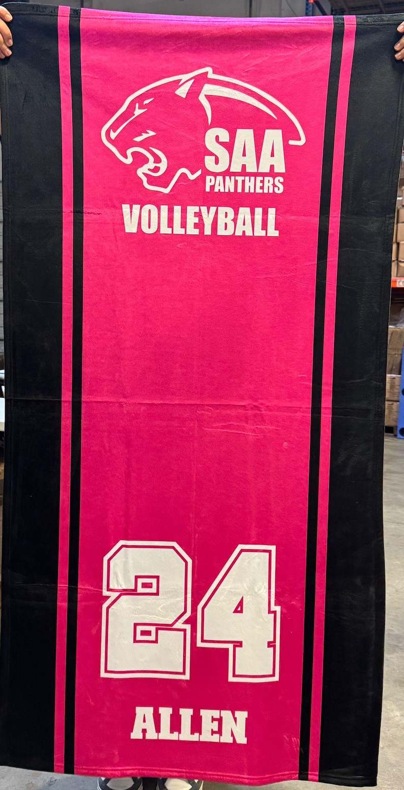 Puede incluir: Una toalla de voleibol rosa con bordes negros y el texto "SAA PANTHERS VOLLEYBALL". La toalla presenta un logotipo de pantera y el n&uacute;mero "24" con el nombre "ALLEN".