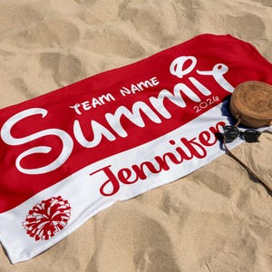 May include: A red and white beach towel with the name "Summit" in large white script, the name "Jennifer" in red script, and a pom-pom graphic. A woven bag and sunglasses rest on the sand next to the towel.