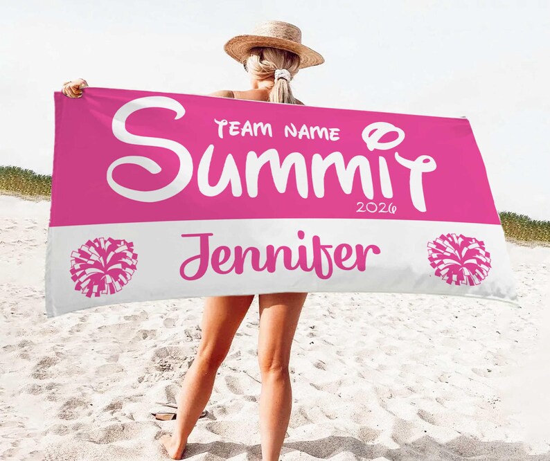 May include: A pink and white personalized beach towel with the name "Summit" in large white script, along with "Jennifer" and the year "2020". The towel features pom-pom graphics on each end.