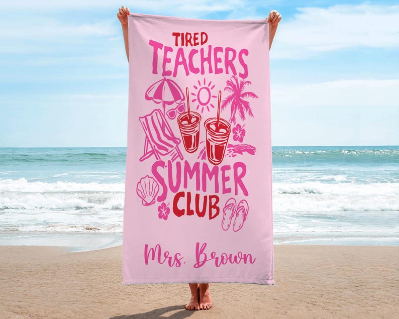 May include: A pale pink beach towel with the text "Tired Teachers Summer Club" in pink and red. The towel features illustrations of a beach chair, sunglasses, drinks, and a palm tree. The name "Mrs. Brown" is printed at the bottom.