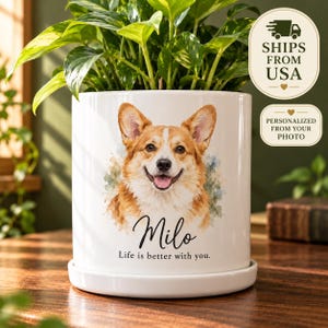 May include: A white ceramic cylindrical planter with a matching saucer featuring a watercolor illustration of a Corgi dog. Below the dog, the name Milo is printed in black script, followed by the text Life is better with you.