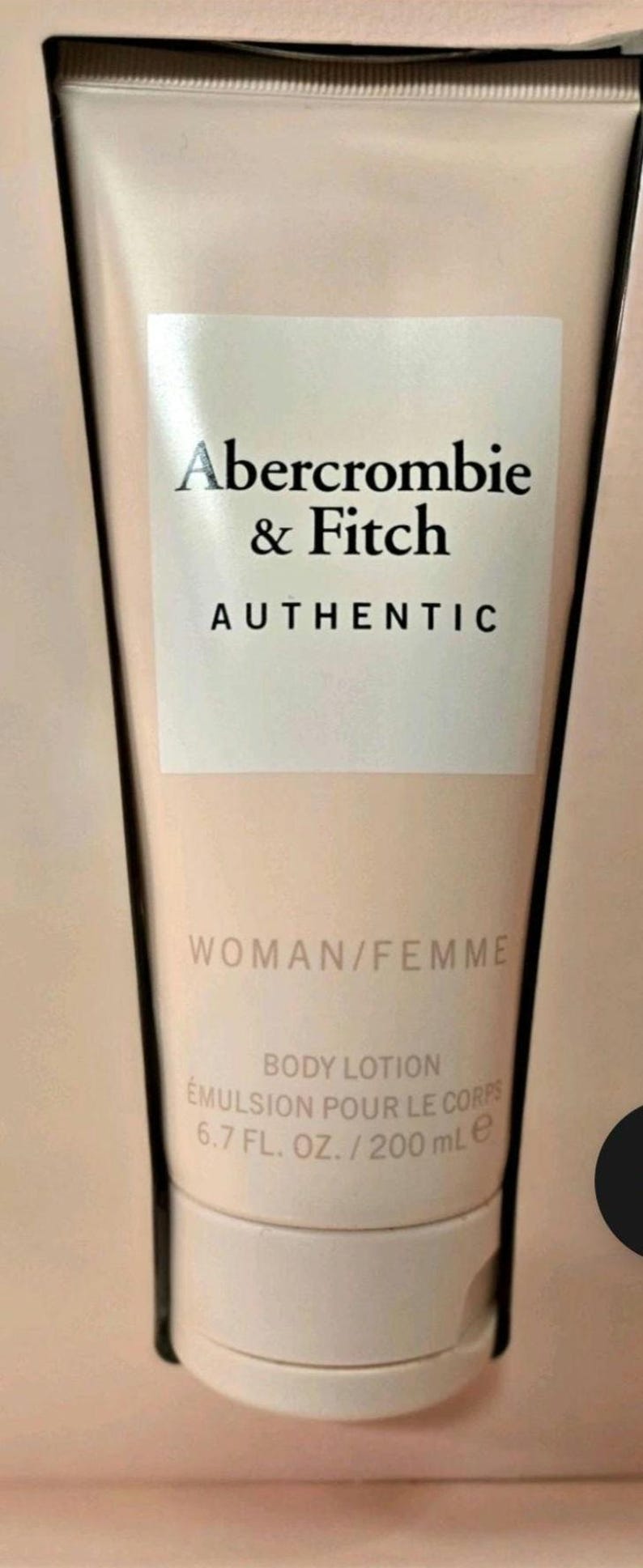 Może przedstawiać: Beżowa tubka balsamu do ciała z logo Abercrombie & Fitch i czarnym napisem "AUTHENTIC". Etykieta zawiera r&oacute;wnież napisy "WOMAN/FEMME" i "BODY LOTION EMULSION POUR LE CORPS 200 ml e."