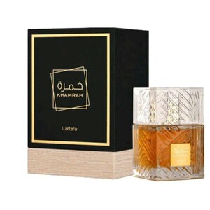 May include: A square glass perfume bottle with a textured geometric pattern containing amber liquid and a gold label reading Khamrah, positioned next to a black rectangular box with gold trim and the text Khamrah and Lattafa in gold.