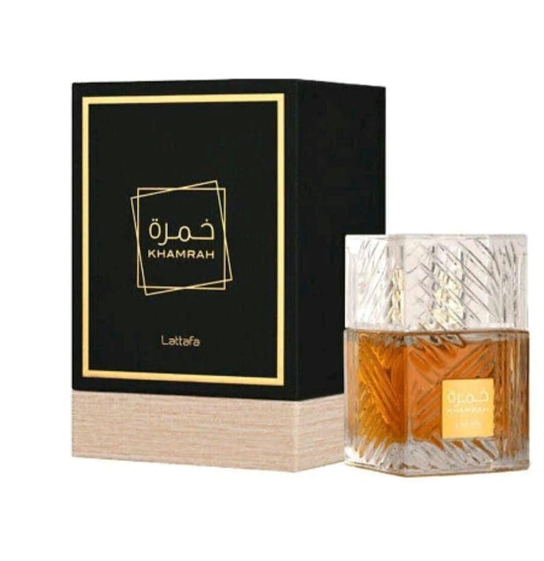 May include: A square glass perfume bottle with a textured geometric pattern containing amber liquid and a gold label reading Khamrah, positioned next to a black rectangular box with gold trim and the text Khamrah and Lattafa in gold.