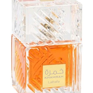 May include: A square glass perfume bottle with a clear, textured, faceted exterior and a matching heavy cap. The bottle contains an amber-colored liquid and features a gold-colored square label on the front with the text Khamrah Lattafa.