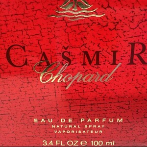 May include: A close-up of a red perfume box with the text "CASMIR Chopard" in gold lettering. The box also features the text "EAU DE PARFUM NATURAL SPRAY VAPORISATEUR" and "3.4 FL OZ e 100 ml".