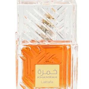 May include: A rectangular glass perfume bottle with a textured, faceted surface containing amber-colored liquid. A square gold label on the front features the text "KHAMRAH Lattafa" in English and Arabic script. The bottle has a clear, matching glass cap.