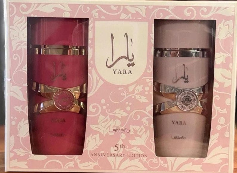 Peut inclure: Coffret cadeau de parfum avec deux flacons. L'un est rose fonc&eacute;, l'autre rose clair, tous deux avec des d&eacute;tails dor&eacute;s et argent&eacute;s. Les flacons portent l'inscription arabe "Yara". La bo&icirc;te rose porte l'inscription "5th Anniversary Edition".