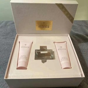 May include: A white gift box with a gold ribbon and the words "Intimately Beckham" on the lid. The box contains a bottle of perfume and two bottles of body lotion.