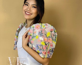 May include: A white crop top with a floral embroidered sheer overlay on the sleeves. The embroidery features pink, yellow, and blue flowers.